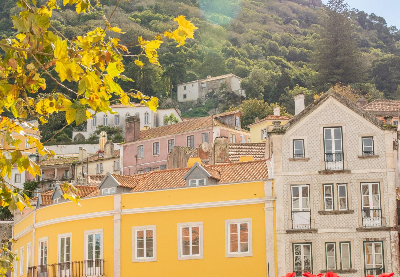 Scenic view of Sintra with historic colorful buildings, red flowers, and a hilltop castle in the background.