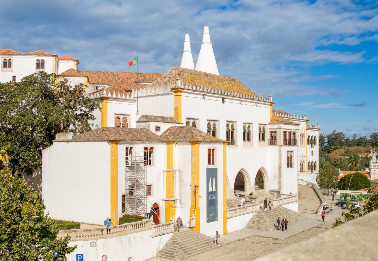 Facade of the National Palace of Sintra, featuring its iconic white chimneys and medieval architecture, under a blue sky.