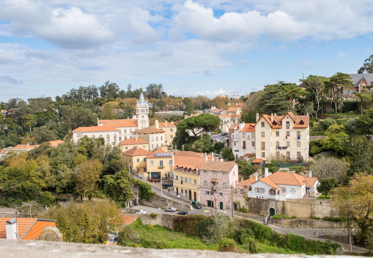Aerial view of Sintra with pastel-colored historic buildings, winding streets, and rolling hills covered in greenery.