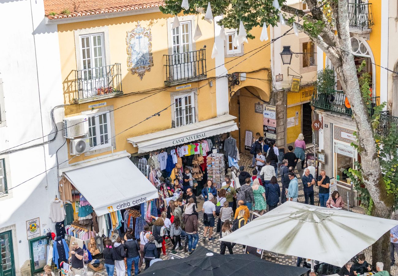 Aerial view of a busy street in Sintra, featuring outdoor cafés, umbrellas, and tourists exploring shops and restaurants.