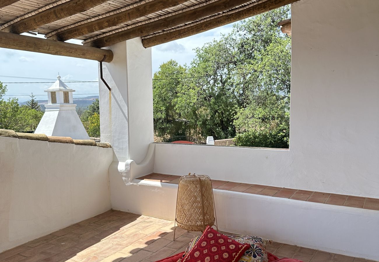 Cozy covered terrace featuring a red mattress, decorative cushions, and a scenic view of the surrounding greenery.
