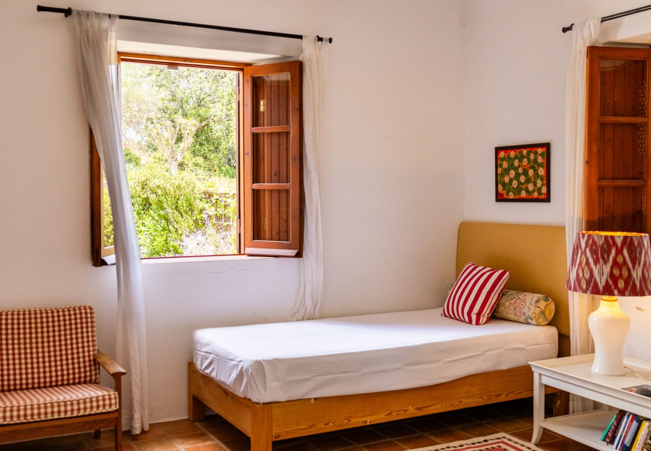 Bedroom decorated with two single beds with yellow headboards, striped pillows, a patterned lamp, a nightstand with books and decorative objects, and 