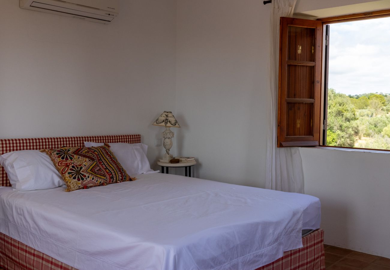 Cozy bedroom with a double bed, decorative pillows, and an open window overlooking nature.