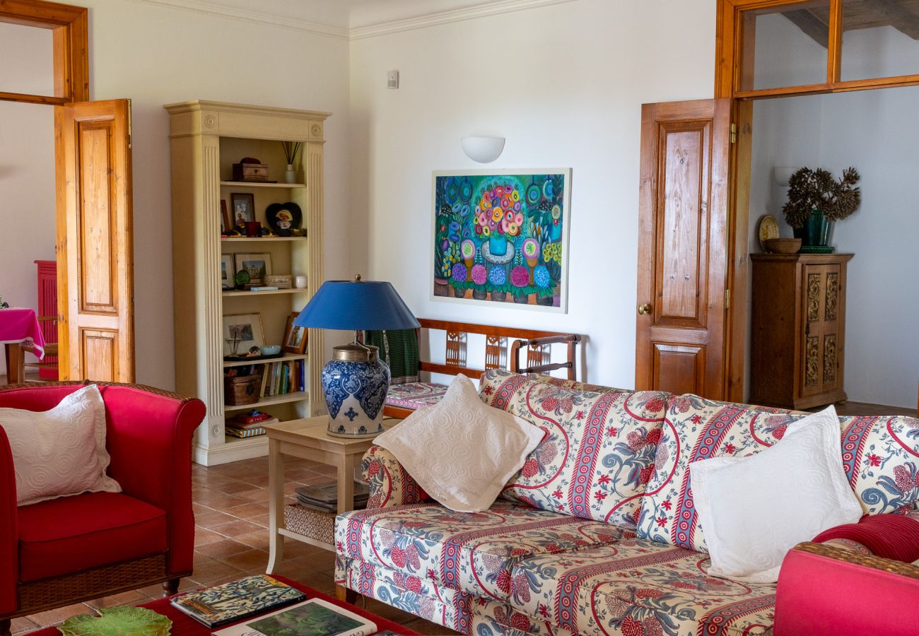  Spacious living room with a floral sofa, red armchairs, a bookshelf, and rustic decor in Almancil.