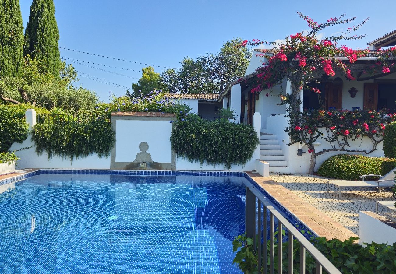 Blue-tiled pool surrounded by a lush garden and a flowered terrace in a villa in Almancil.