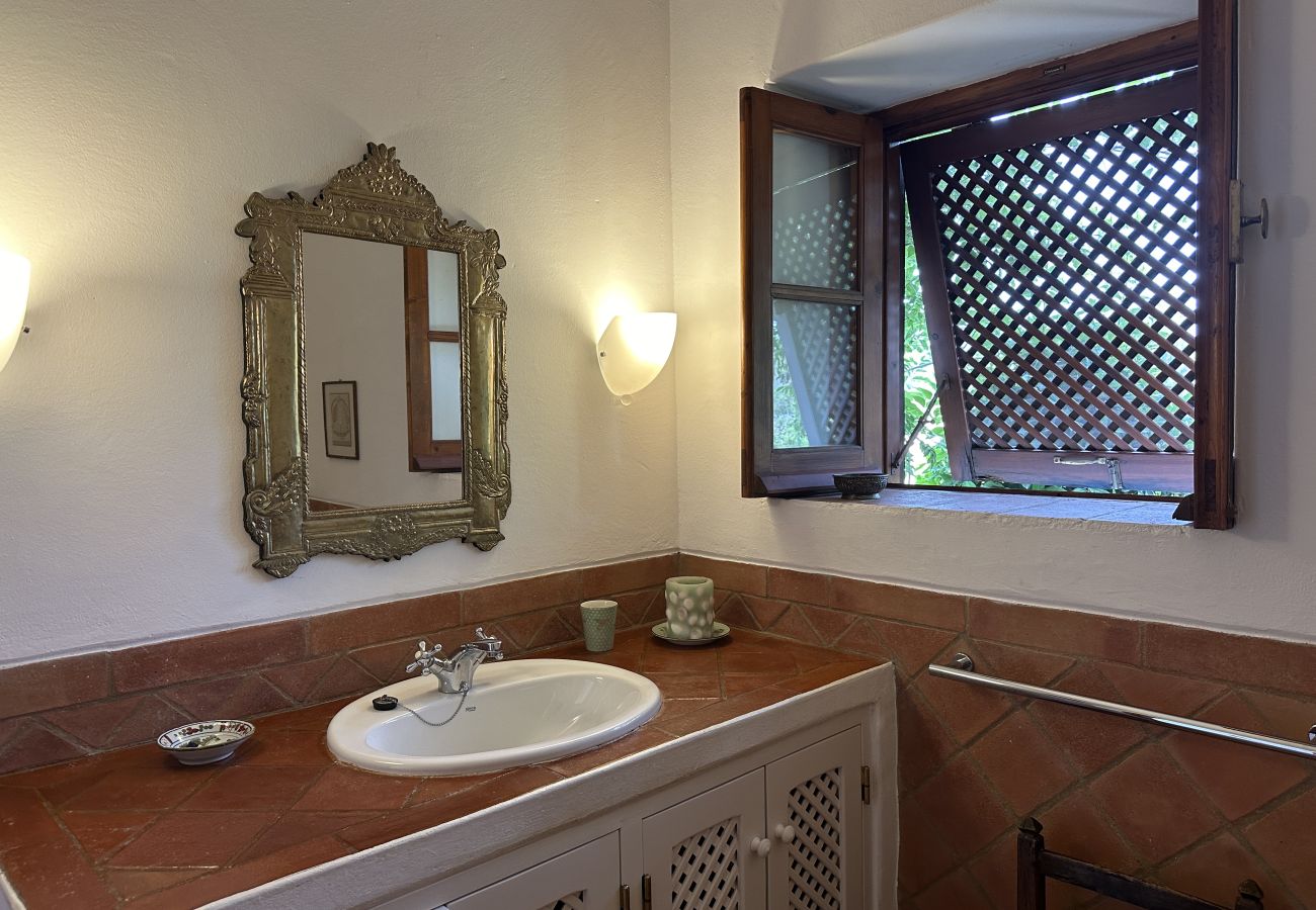 Charming bathroom with a rustic tiled countertop, ornate mirror, cozy wall lighting, and a wooden lattice window providing ventilation and natural lig