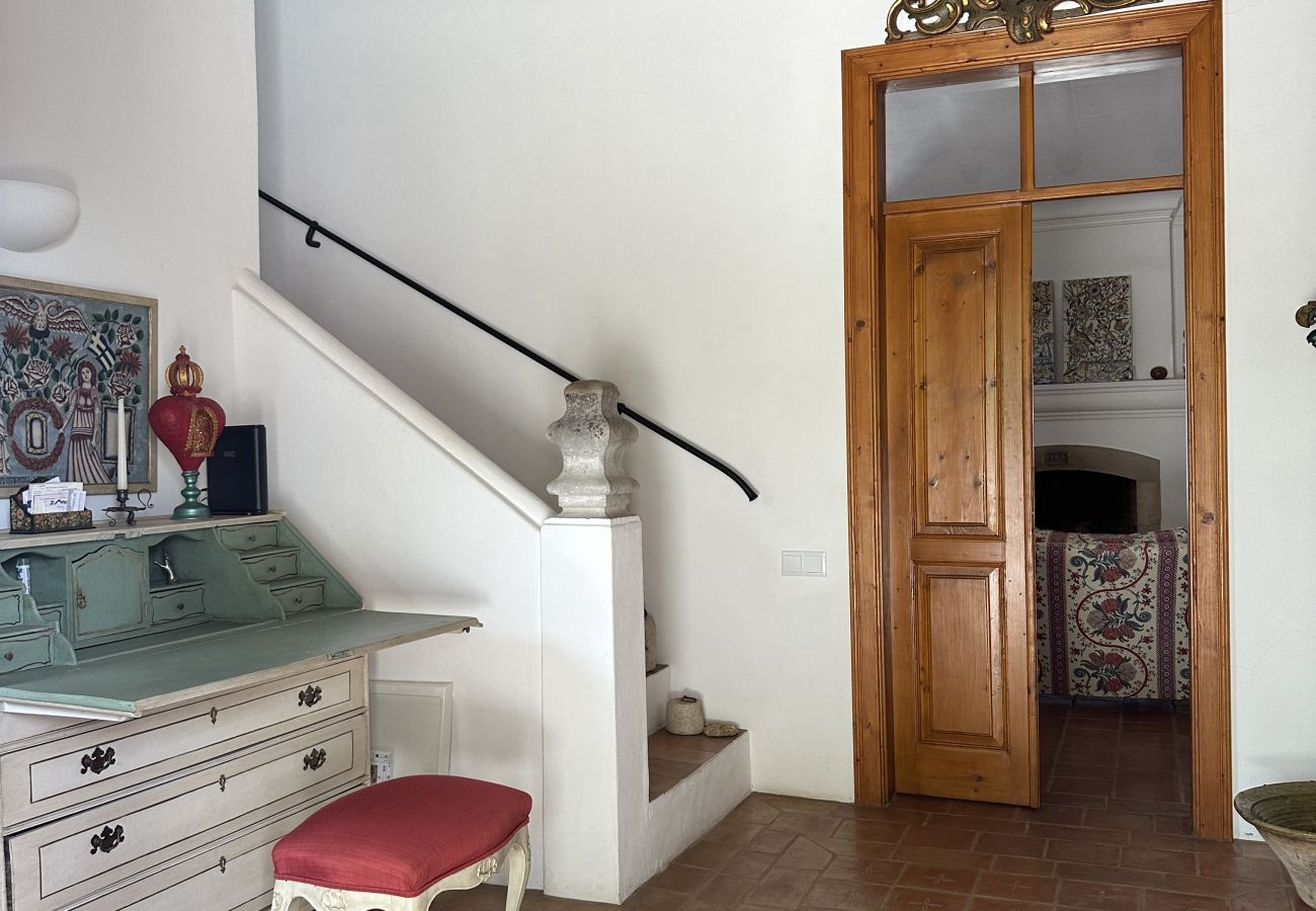 Bright reception area with classic furniture, including a green writing desk and upholstered stool, featuring a staircase leading upstairs and an open