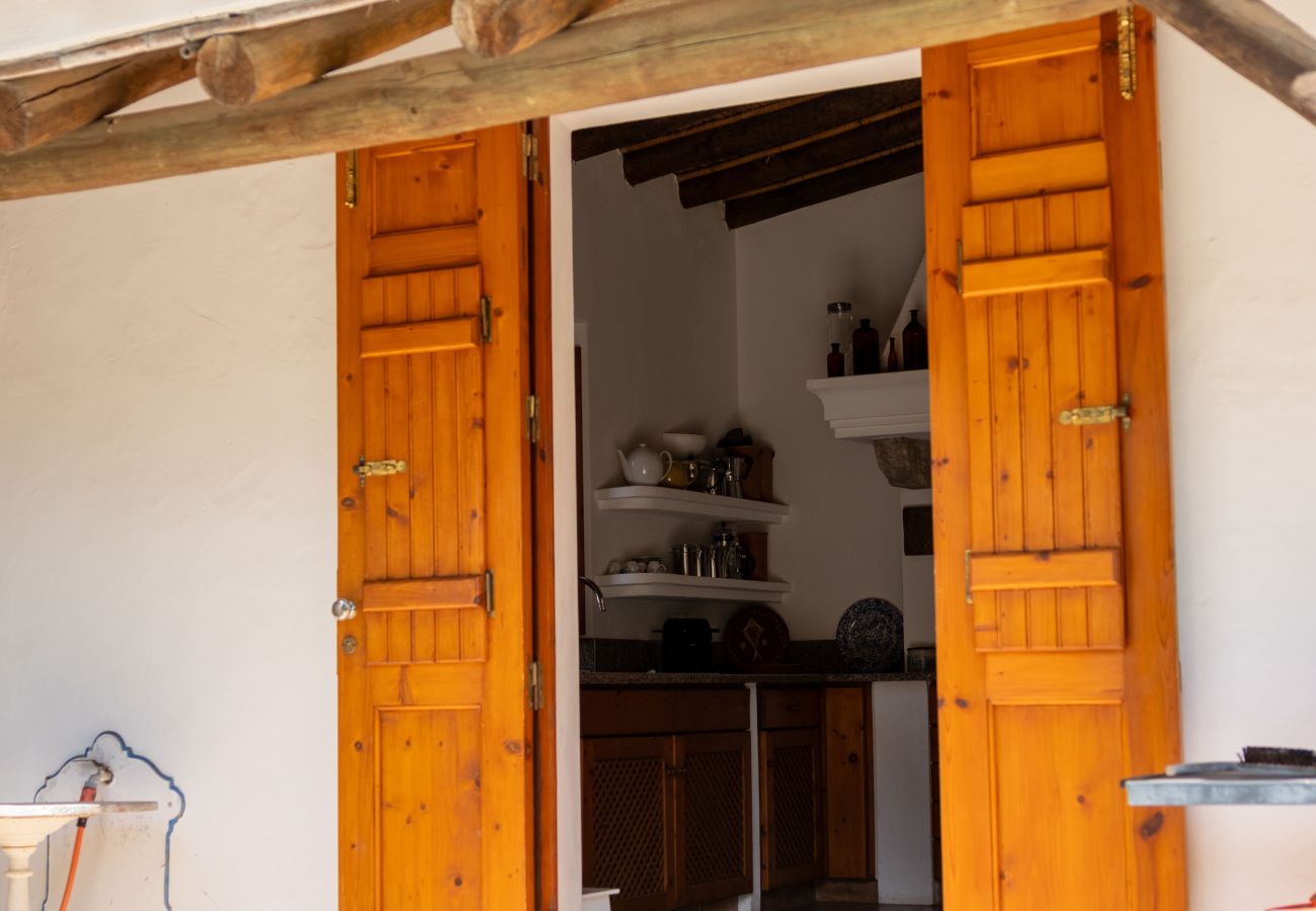Rustic double wooden door open, revealing the interior of a traditional kitchen with wooden shelves and countertop, under a ceiling with exposed beams