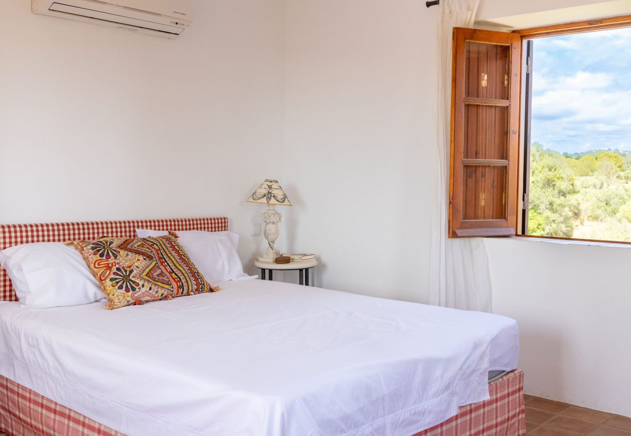 Cozy bedroom with a double bed, decorative pillows, and an open window overlooking the green landscape.