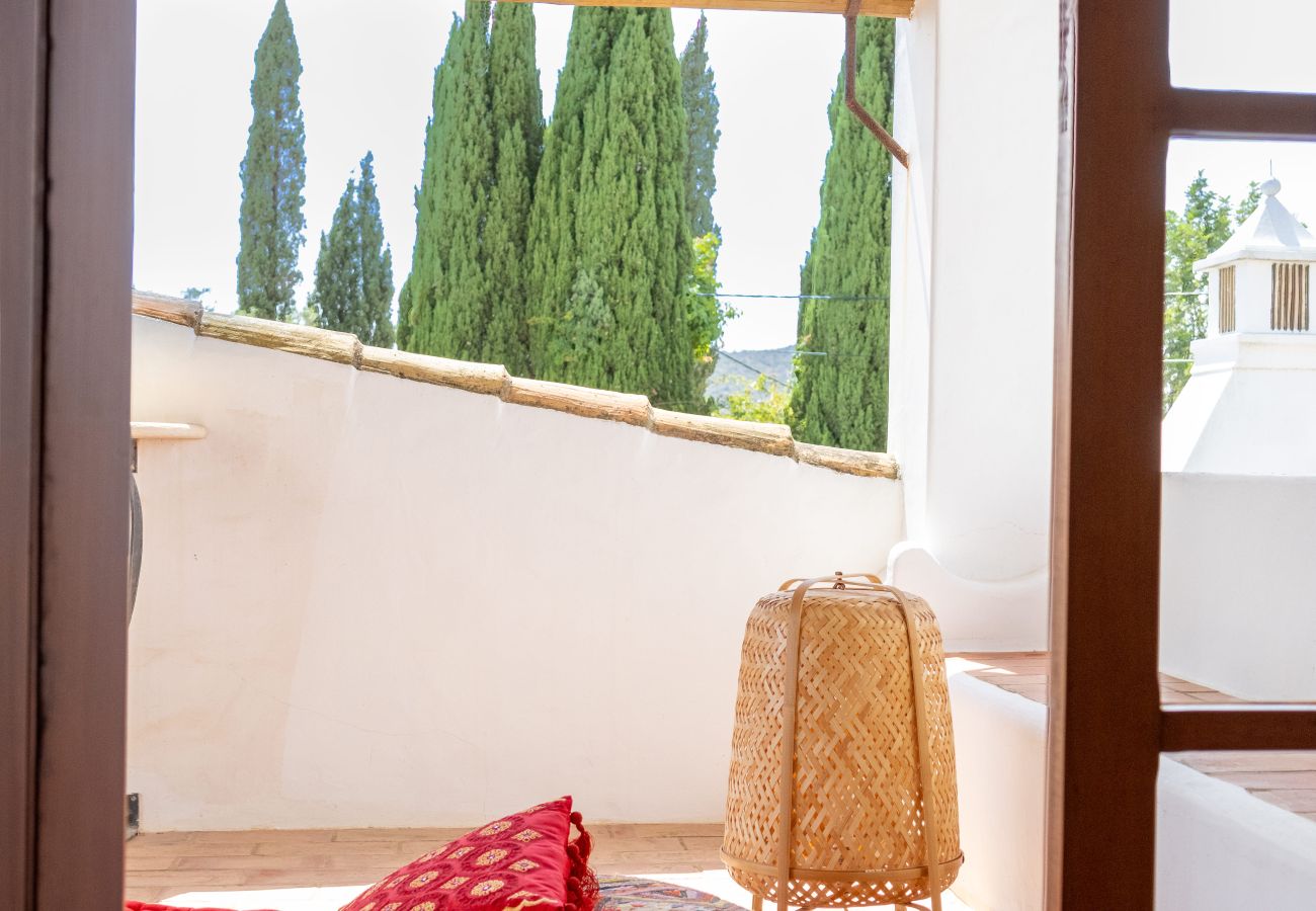 Cozy covered terrace featuring a red mattress, decorative cushions, and a scenic view of the surrounding greenery.