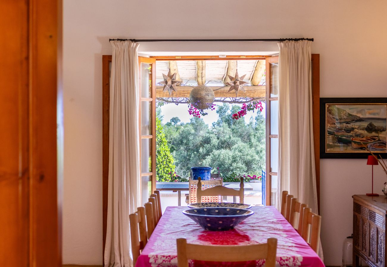 Cozy dining room with a wooden table, colorful tablecloth, and open doors leading to a flower-filled terrace in Almancil.