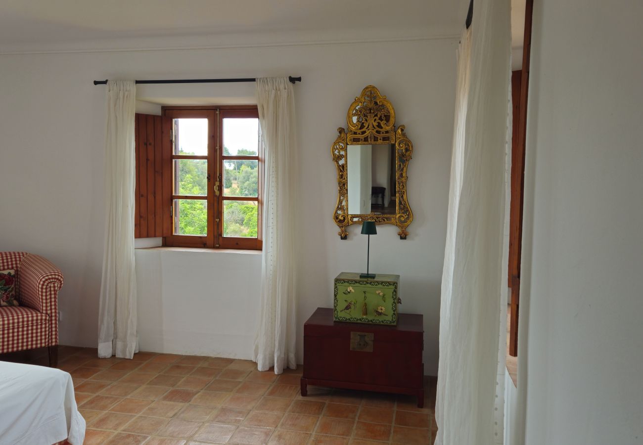 Bedroom decorated with a checkered armchair, golden mirror, and an open window revealing a lush green landscape.