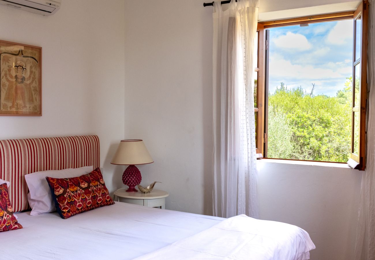 Comfortable bedroom with a double bed, striped headboard, decorative pillows, elegant bedside lamp, and an open wooden window with light white curtain