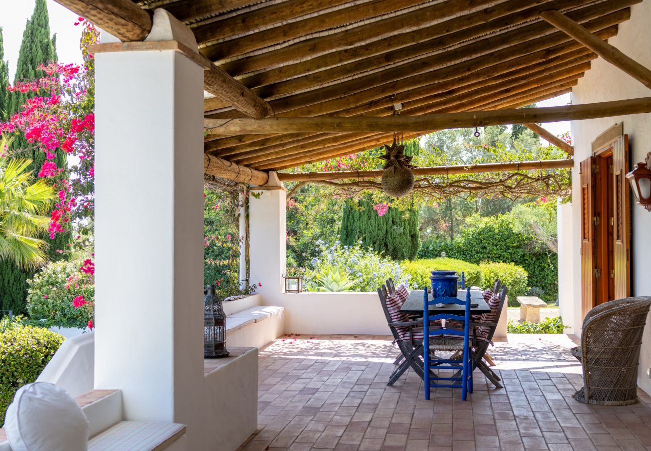 Spacious terrace with a blue dining table, rustic wooden ceiling, and a lush garden view in Almancil.