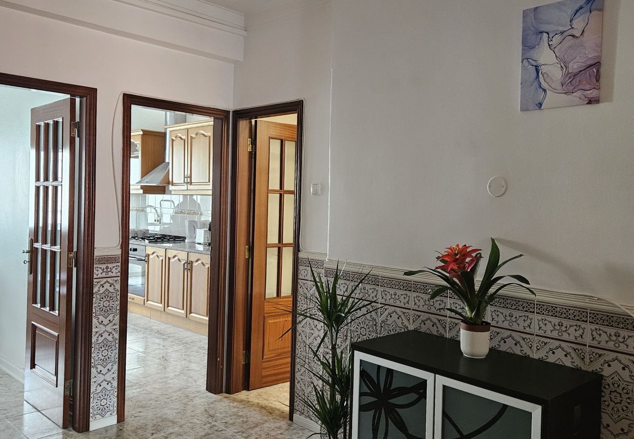 Entrance to the kitchen with double glass doors, decorative tiled wall, modern black cabinet, plants, and a vase with colorful flowers.
