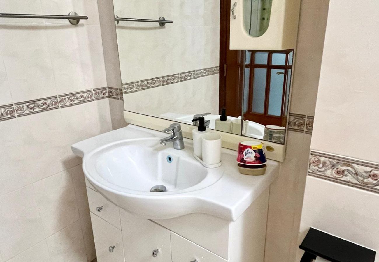 Bathroom featuring beige tiles with decorative accents, a large mirror, white sink with built-in cabinet, bidet, toilet, and bathtub with glass partit