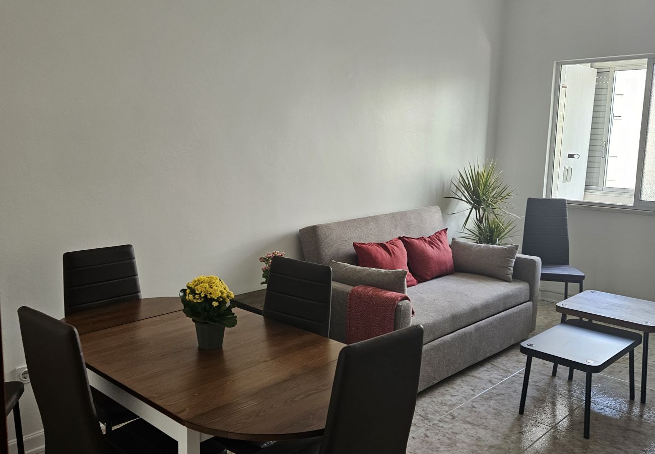 Bright living room featuring a gray sofa, red cushions, a dining table for four, and minimalist decor.