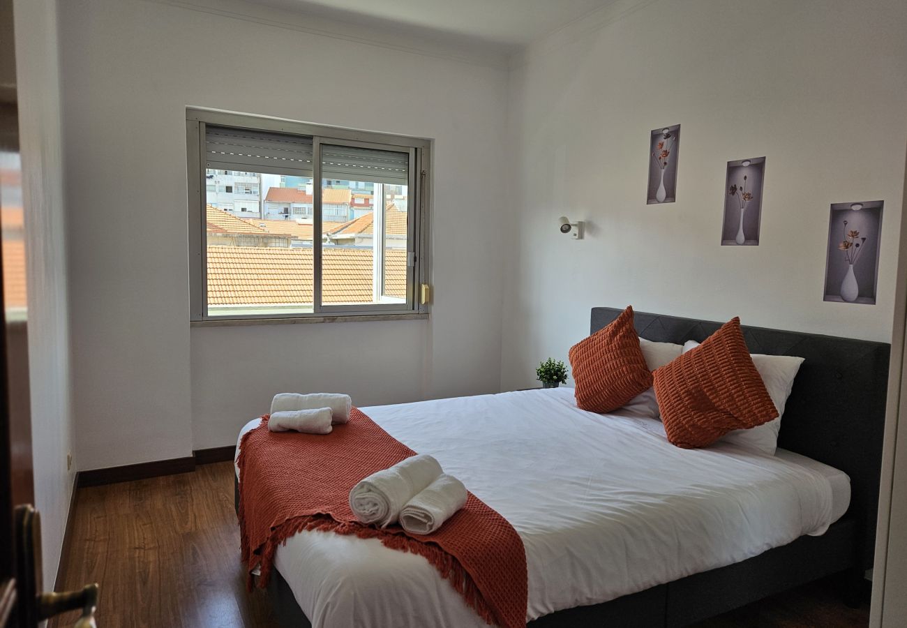Comfortable bedroom featuring a double bed, white bedding, terracotta-colored pillows and throw, wooden flooring, and a wall decorated with artistic p