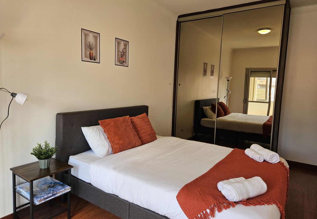 Stylish bedroom featuring a double bed, upholstered headboard, white bedding with orange accents, a large wall mirror, and soft lighting.