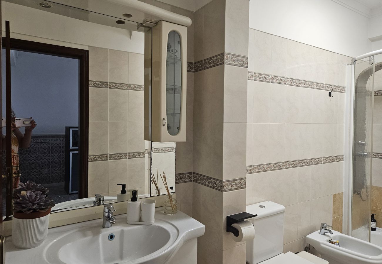 Bathroom featuring beige tiles with decorative accents, a large mirror, white sink with built-in cabinet, bidet, toilet, and bathtub with glass partit