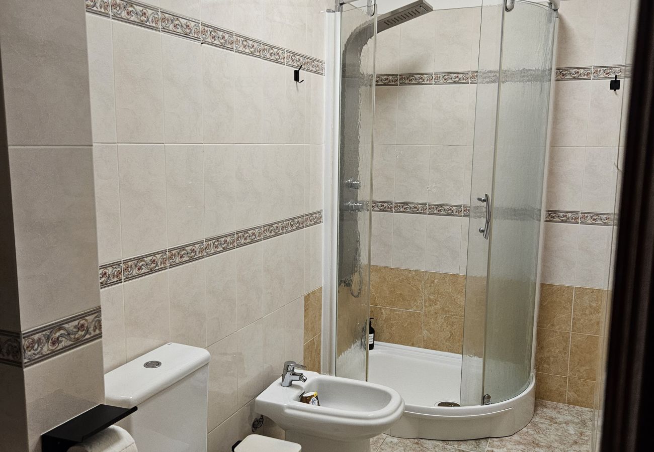 Bathroom featuring beige tiles with decorative accents, a large mirror, white sink with built-in cabinet, bidet, toilet, and bathtub with glass partit