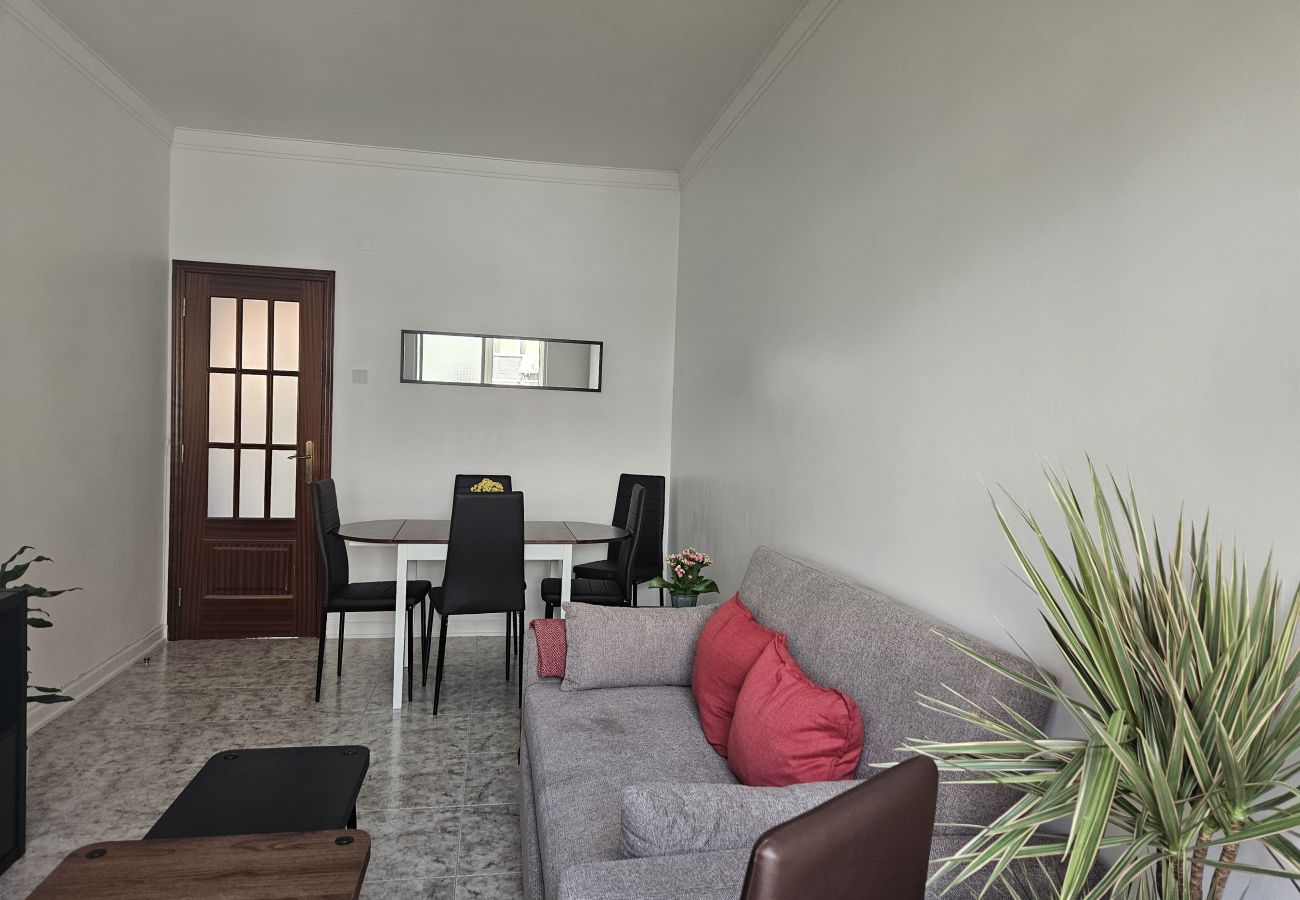 Spacious living room featuring a gray sofa, red cushions, decorative plant, dining table for four, and a wall mirror.