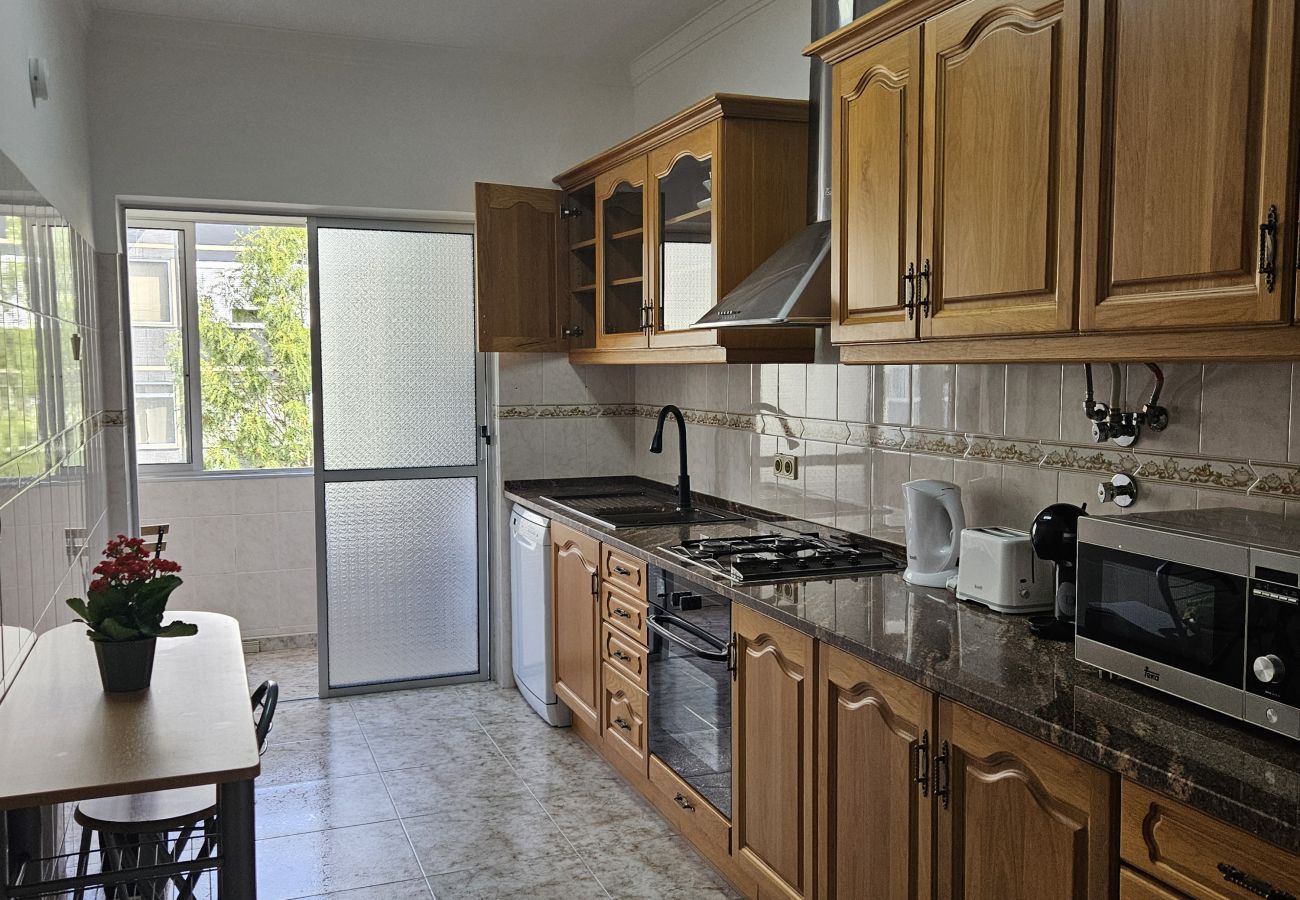 Large kitchen with wooden cabinets, modern appliances, a dining table, and a glass door leading to the balcony.