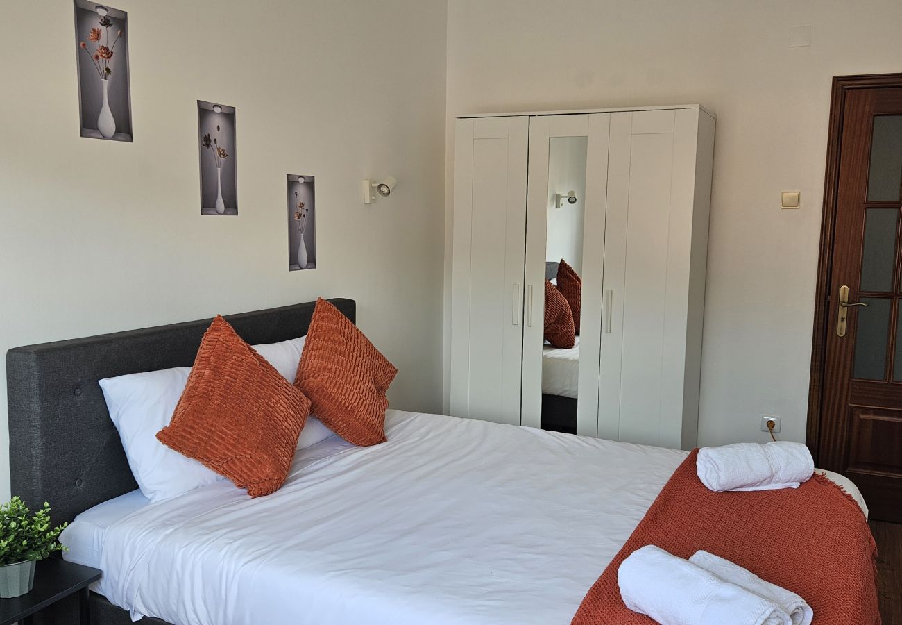 Stylish bedroom featuring a double bed, upholstered headboard, white bedding with orange accents, a large wall mirror, and soft lighting.