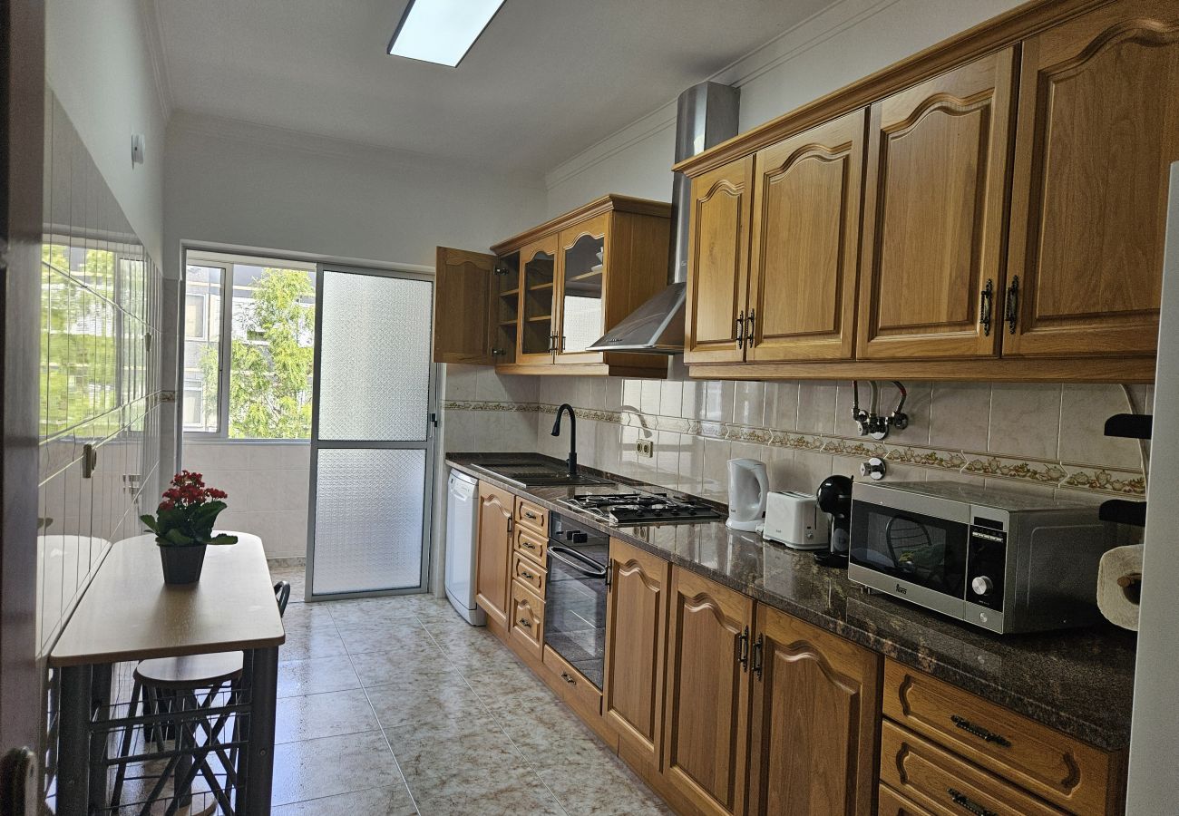 Large kitchen with wooden cabinets, black countertop, modern appliances, and a side table near the glass door with an outdoor view.