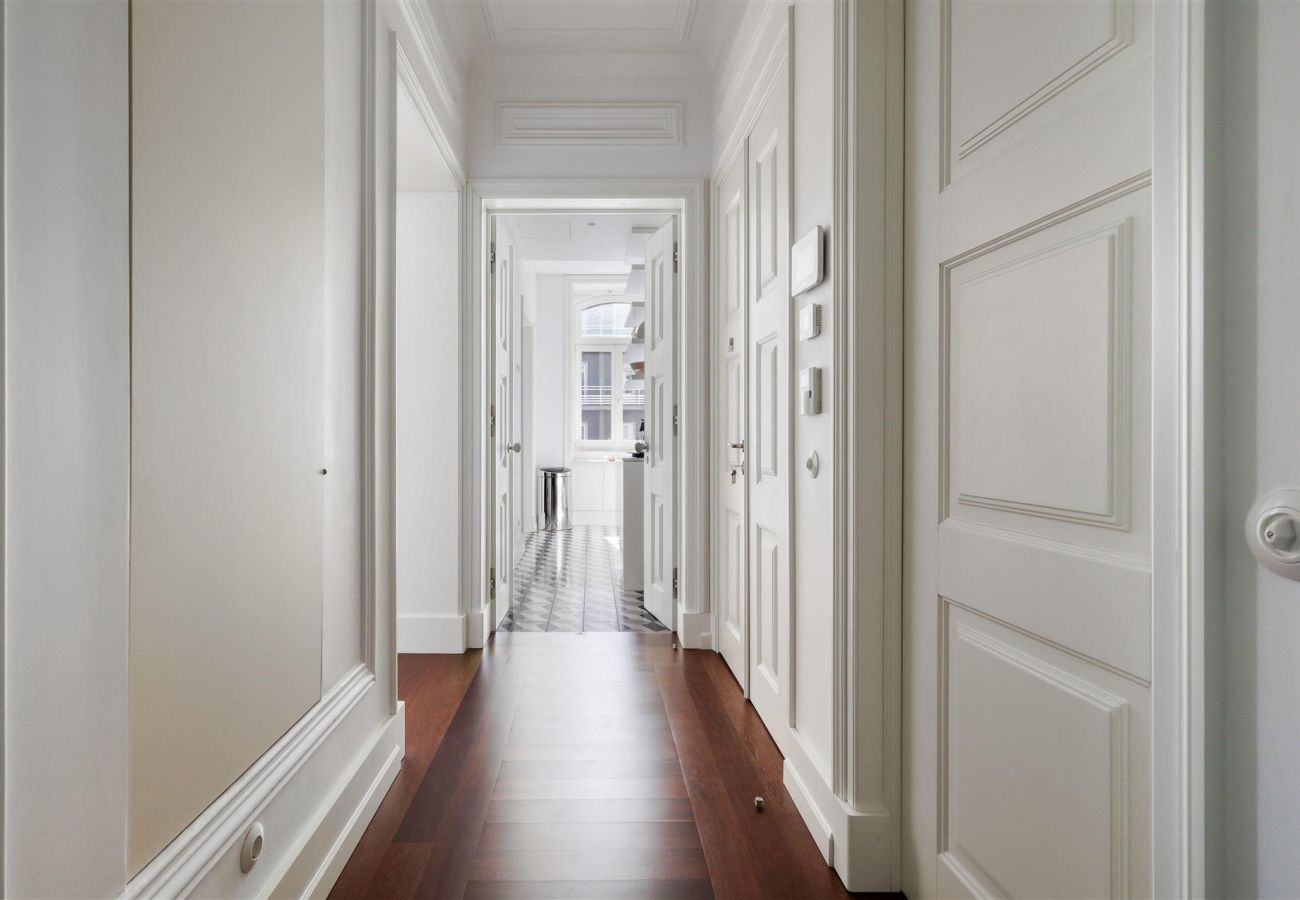  Elegant hallway with wooden flooring, classic white doors, and natural lighting in the background.