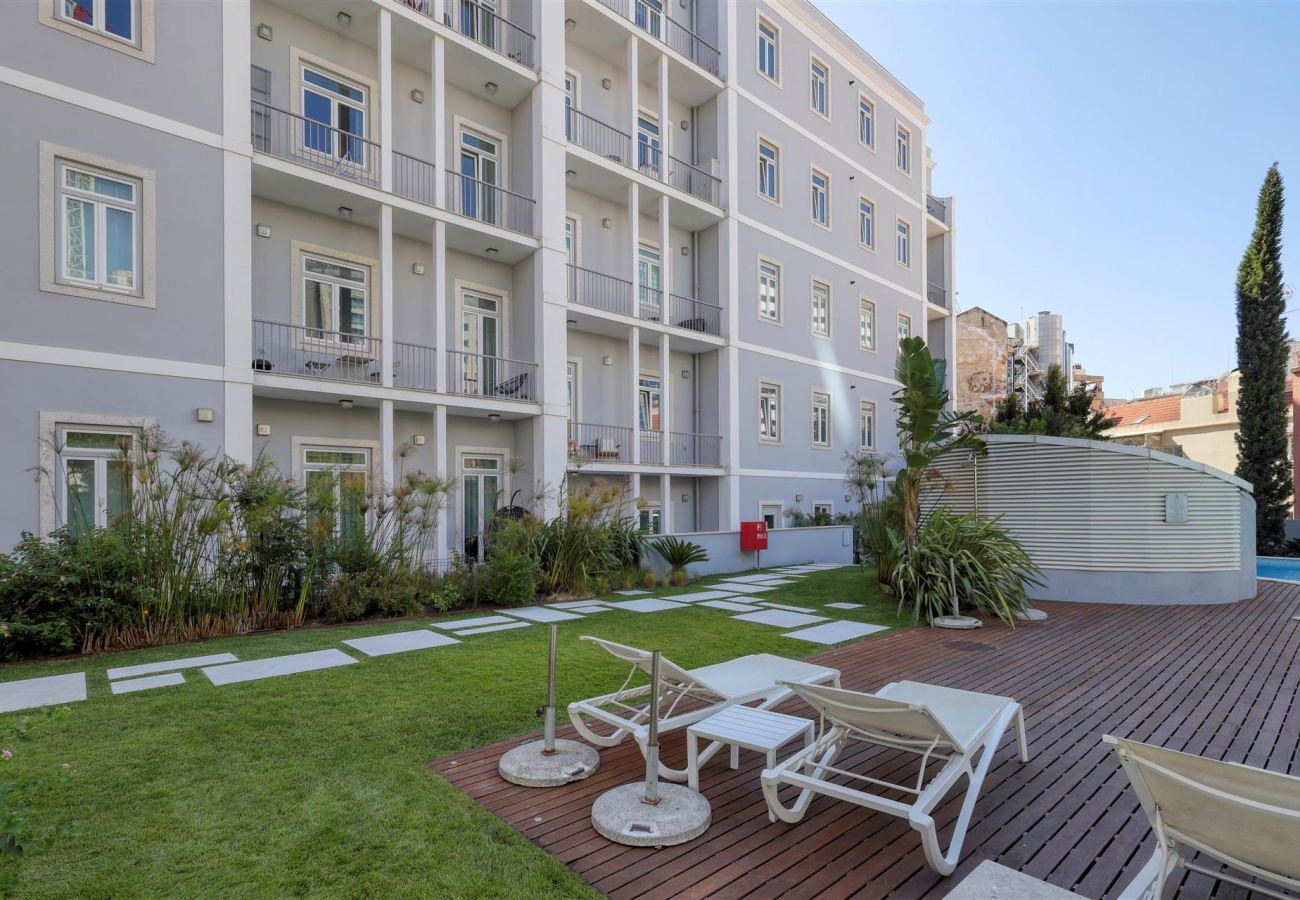 Outdoor space with sun loungers on a wooden deck, surrounded by well-kept gardens and elegant architecture.
