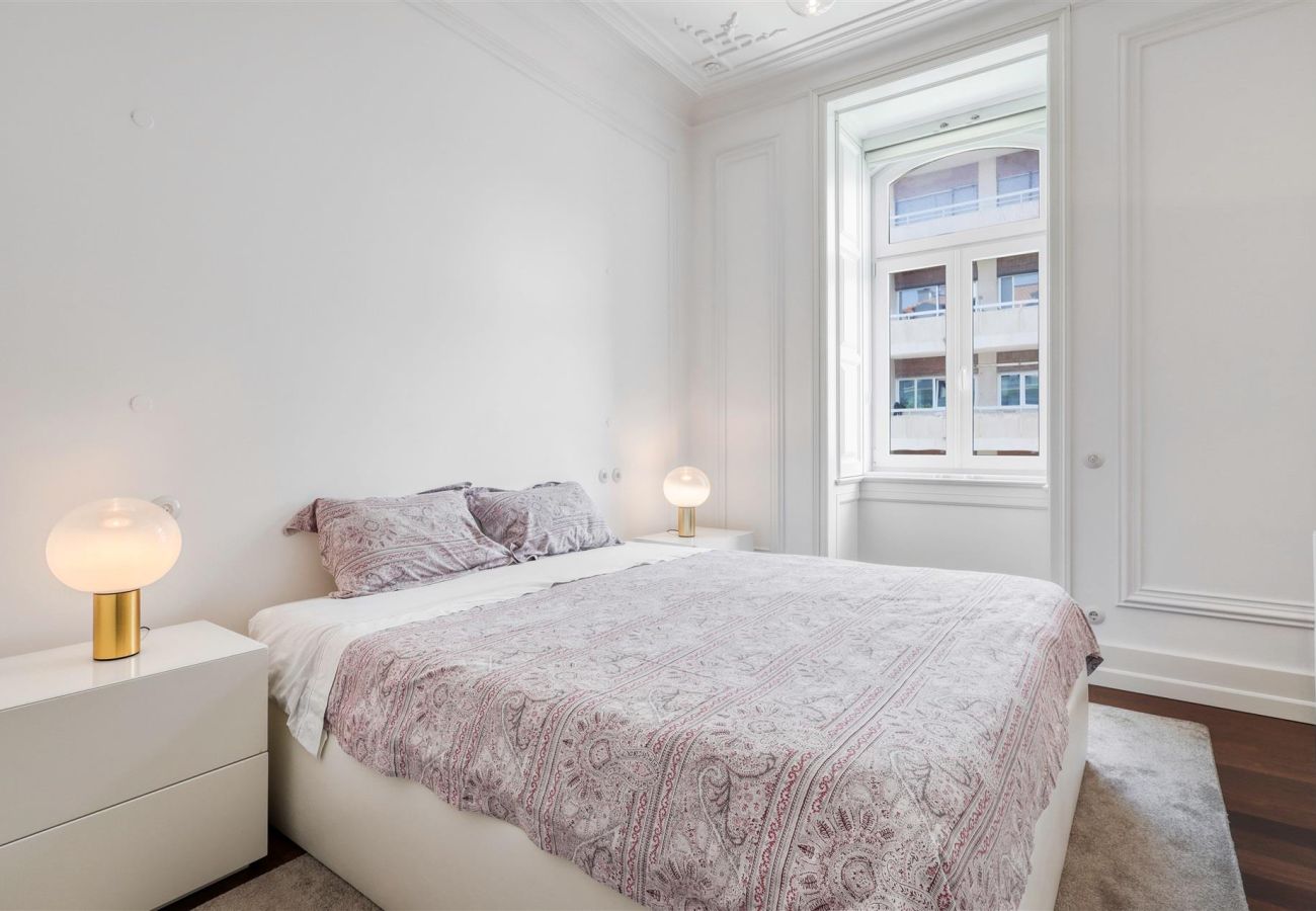Elegant bedroom with double bed, lilac bedding, natural light, and minimalist decor.
