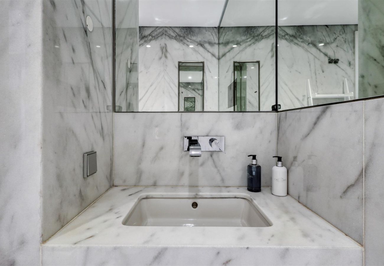 Modern white marble washbasin with a large mirror, built-in faucet, and hygiene items.
