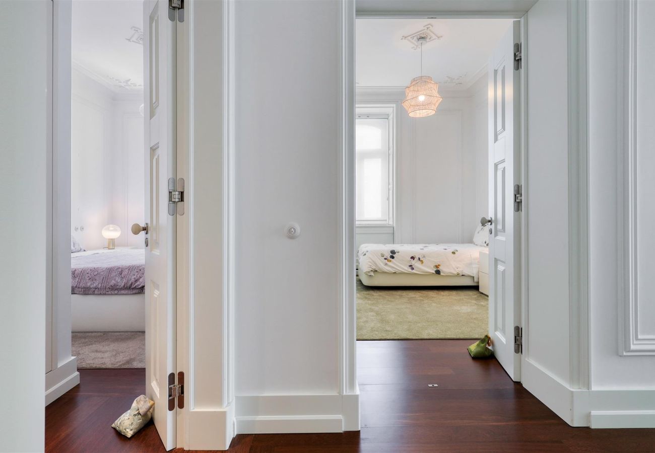  Sophisticated hallway with white walls and wooden flooring, leading to a cozy bedroom with soft lighting.