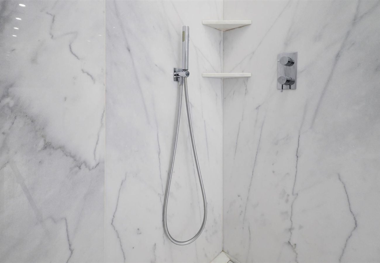 Modern built-in shower on a white marble wall, featuring minimalist shelves and a sophisticated design.