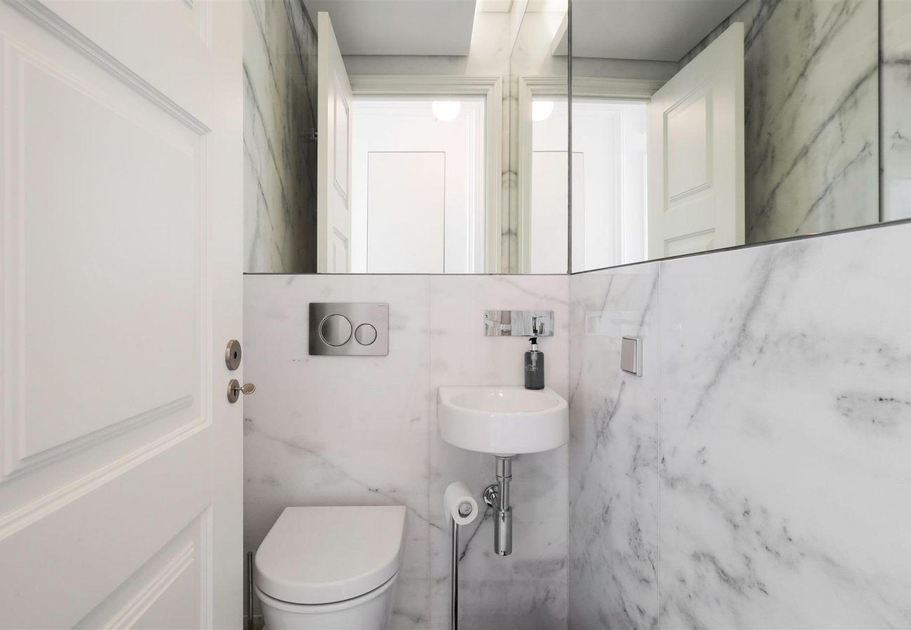 Small bathroom with elegant design, featuring white marble walls, a large mirror, and a compact sink.
