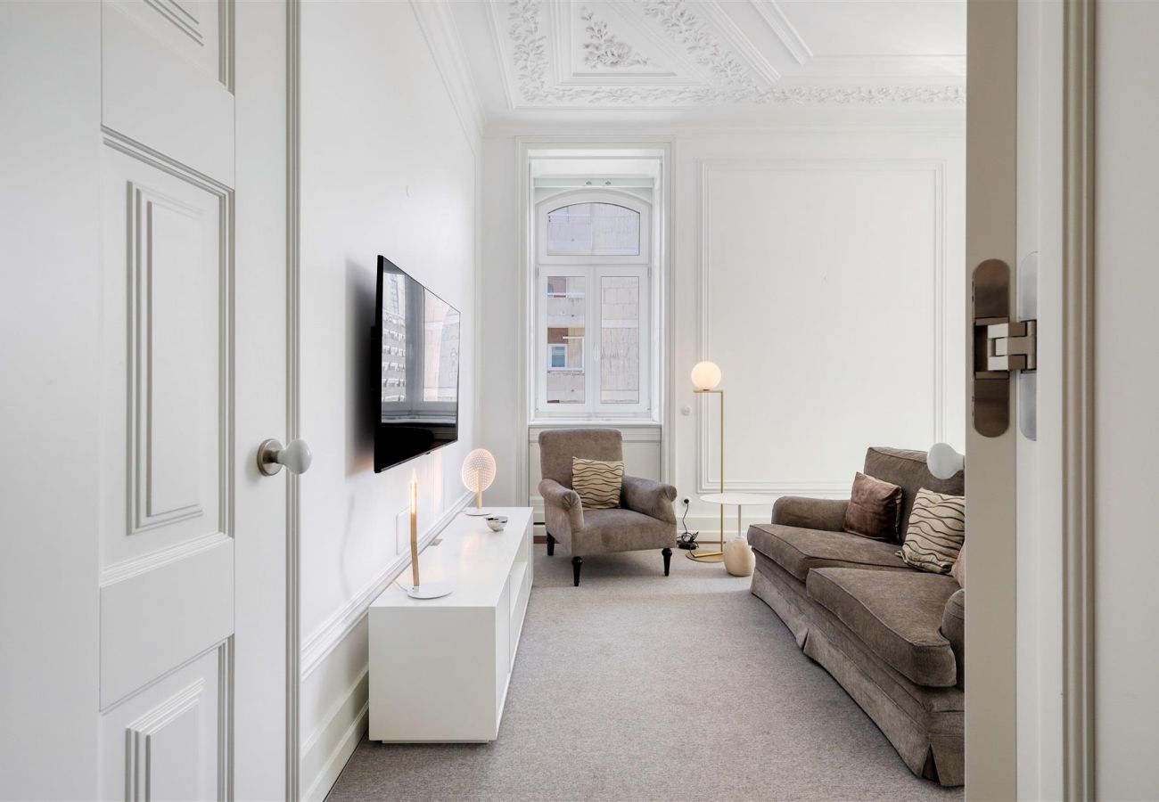Sophisticated living room with a large sofa, armchair, wall-mounted TV, and modern lighting, featuring classic ceiling moldings.