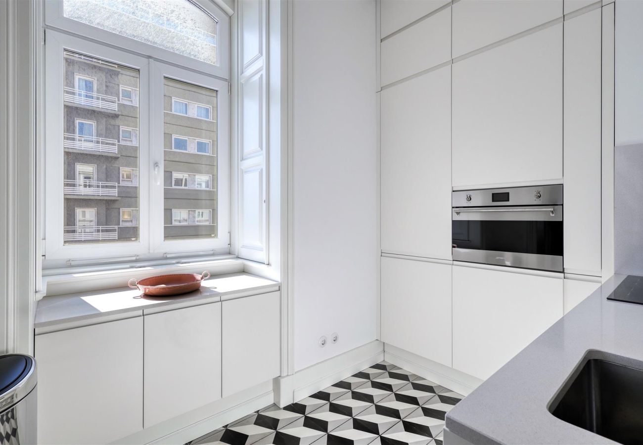 White and sophisticated kitchen with a minimalist design, tall cabinets, built-in oven, and a black and white geometric floor.