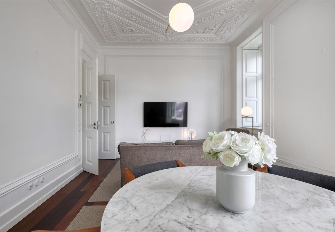 Elegant living room featuring classic ceiling details, marble table with a flower vase, sofa, and wall-mounted TV.