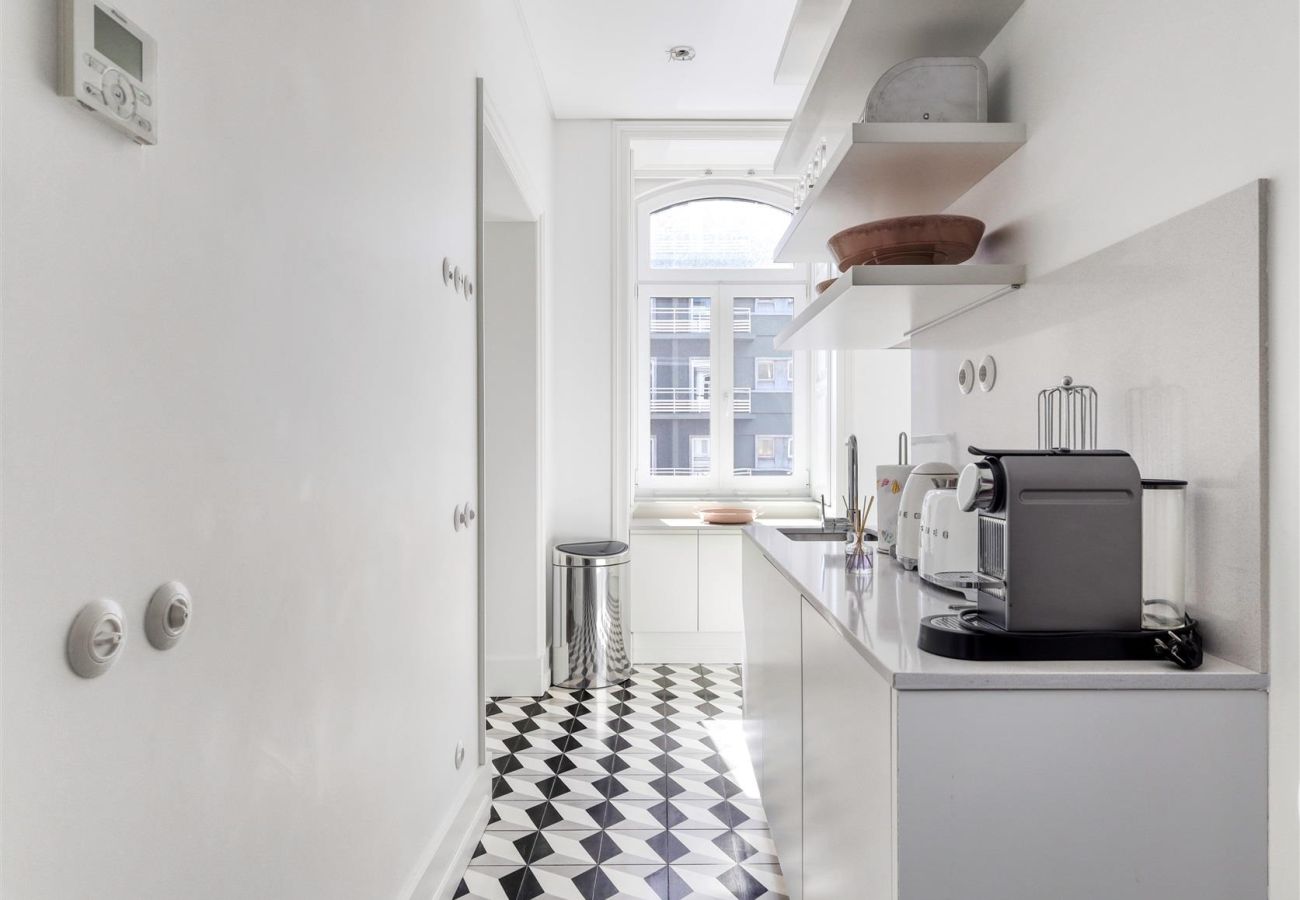Bright and elongated kitchen with modern appliances, open shelves, and a stylish black and white geometric floor.